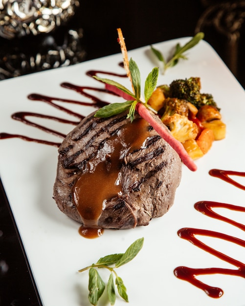 Médaillon de filet de boeuf grillé avec sauce et légumes sur une plaque blanche