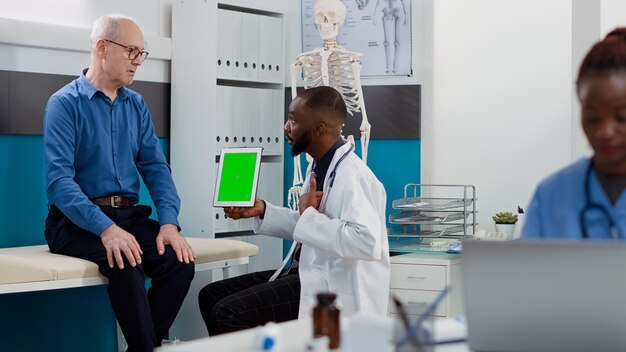 Médecin afro-américain pointant vers une tablette avec écran vert, regardant un modèle chromakey avec un patient âgé. Médecin et homme utilisant un fond de maquette isolé et un espace de copie vierge.
