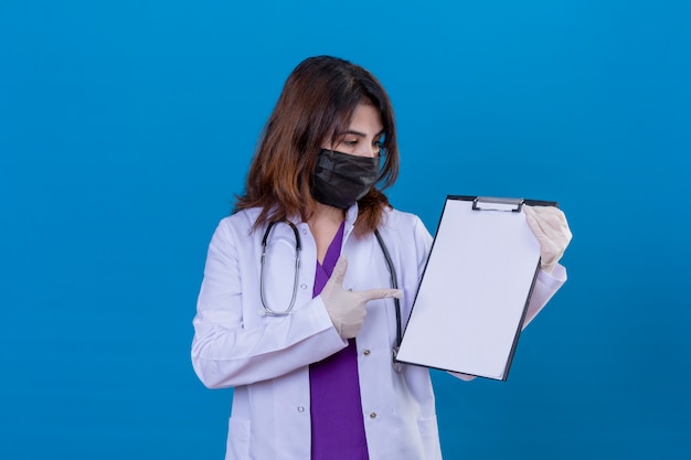 Médecin d'âge moyen portant une blouse blanche dans un masque facial de protection noir et avec un stéthoscope holding clipboard