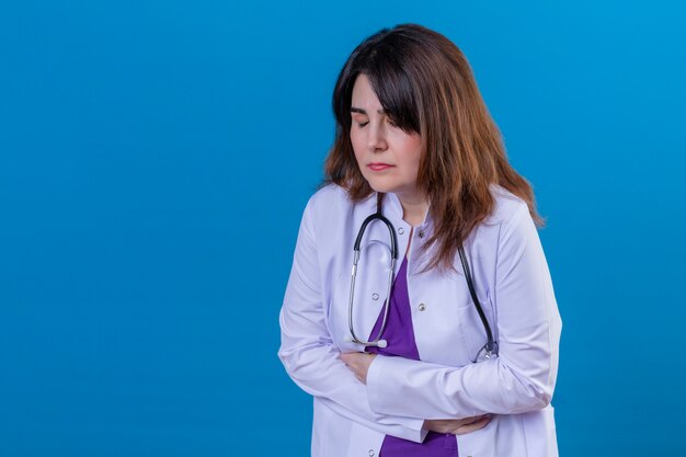 Médecin D'âge Moyen Portant Une Blouse Blanche Et Avec Stéthoscope à L'estomac Mal En Point Souffrant De Douleurs Sur Le Mur Bleu