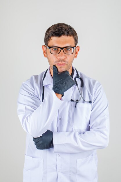 Médecin en blouse blanche avec stéthoscope soutenant le menton sur sa main et à la recherche de concentré