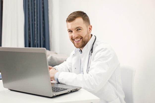 Médecin caucasien assis sur le lieu de travail et utilisant un ordinateur portable