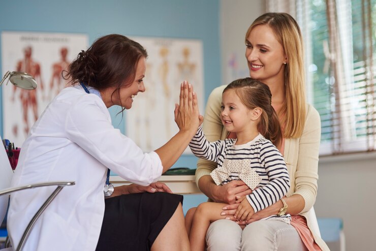 Photo gratuit un médecin donne un haut cinq à une fille souriante assise sur les genoux de sa mère lors d'un rendez-vous médical
