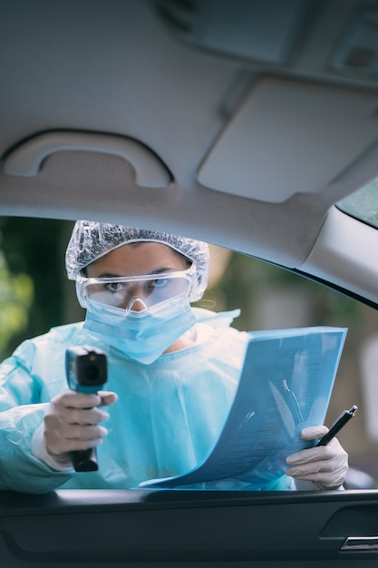 Médecin femme utilise un pistolet thermomètre infrarouge pour vérifier la température corporelle. Pour les symptômes du virus covid-19. Femme avec la robe d'isolement ou des combinaisons de protection et des masques chirurgicaux en plein air.