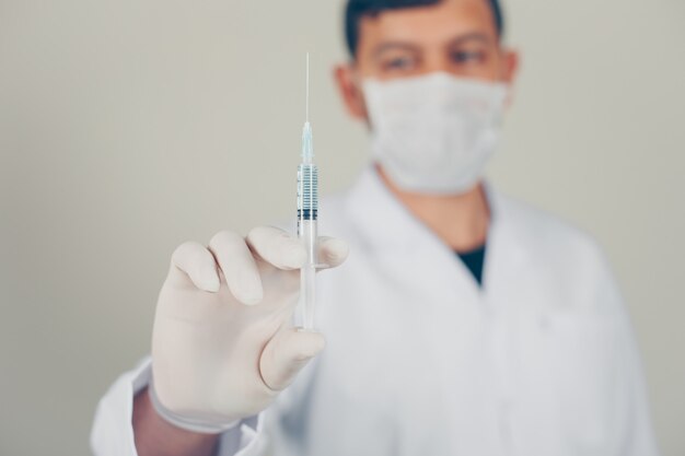 Médecin avec des gants et un masque tenant une seringue. vue de côté.