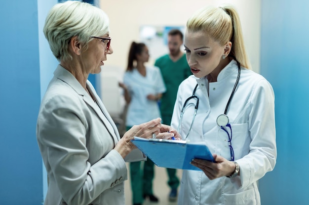 Médecin généraliste et femme mûre analysant les dossiers médicaux et parlant des résultats des tests dans un couloir de la clinique