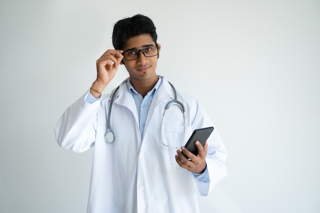 Médecin indien confiant ajustant ses lunettes lors de l&#39;utilisation du smartphone.