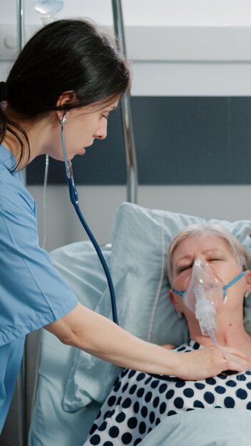 Médecin et infirmière utilisant un masque à tube à oxygène pour un patient âgé souffrant d'une respiration lourde et d'un problème respiratoire dans la salle d'hôpital. Médecins spécialistes traitant une femme malade hyperventilant au lit