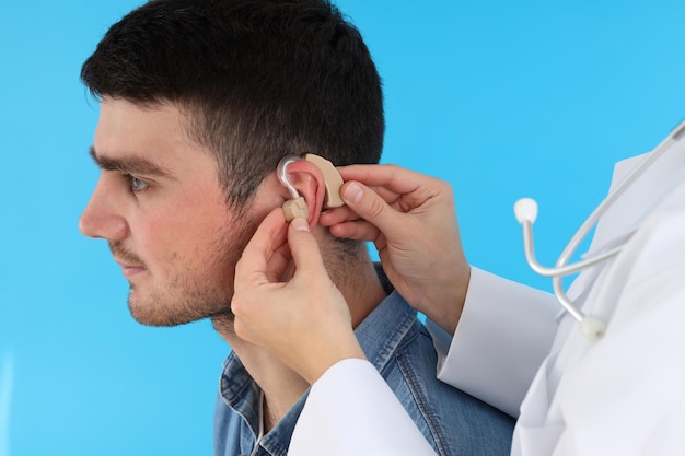 Le médecin installe une prothèse auditive sur l'oreille du jeune homme sur fond bleu
