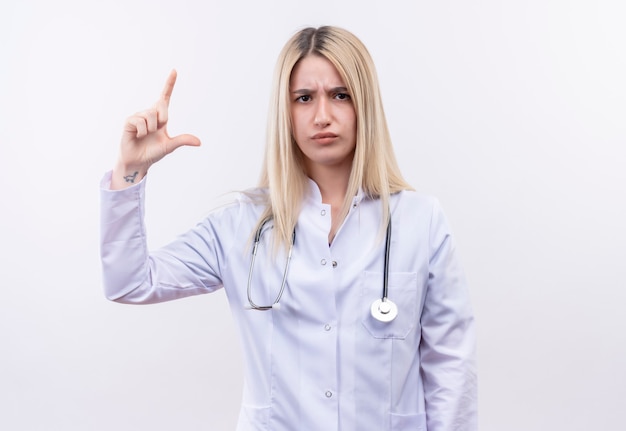 Médecin jeune fille blonde portant un stéthoscope et une robe médicale montrant la taille sur un mur blanc isolé