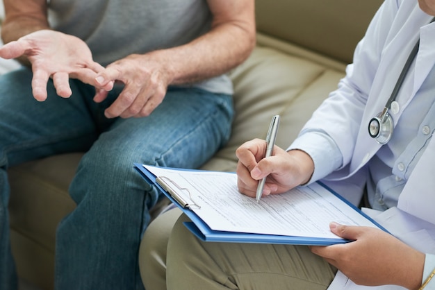 Médecin méconnaissable parlant au patient à la maison et prenant des notes