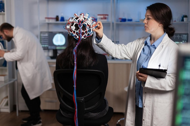 Médecin neurologue spécialiste surveillant l'évolution du cerveau du patient avec un casque eeg sur la tête lors d'une expérience en neurosciences dans un laboratoire moderne. médecin chercheur analysant l'activité du système nerveux
