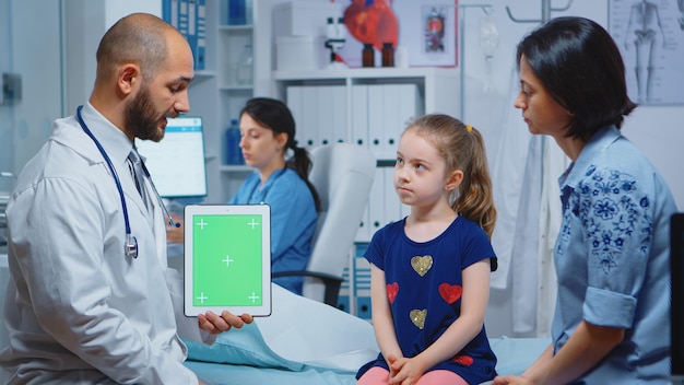 Médecin et patients regardant une tablette à écran vert dans un cabinet médical. Spécialiste de la santé avec écran de remplacement de maquette isolé pour ordinateur portable à clé chroma. Thème médical lié à la médecine facile à saisir.