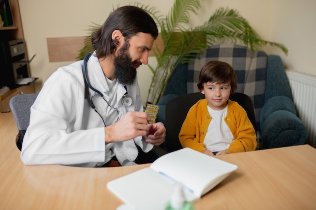 Photo gratuite médecin pédiatre examinant un enfant dans un cabinet médical confortable. concept de soins de santé, enfance, médecine, protection et prévention. le petit garçon fait confiance au médecin et ressent des émotions calmes et positives.