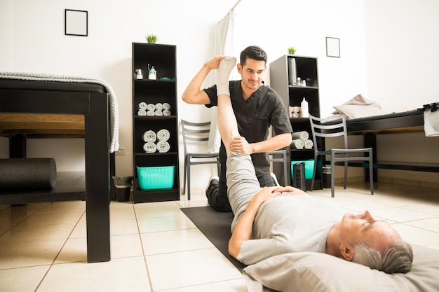 Photo gratuite médecin de physiothérapie aidant un patient âgé à faire de l'exercice pour les jambes en clinique