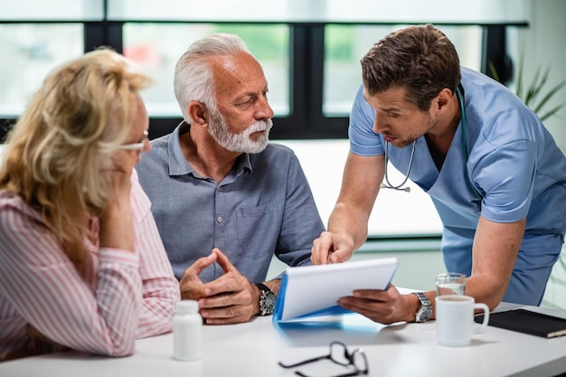 Photo gratuite médecin sérieux discutant avec un couple de personnes âgées de leurs documents médicaux lors d'un rendez-vous à la clinique