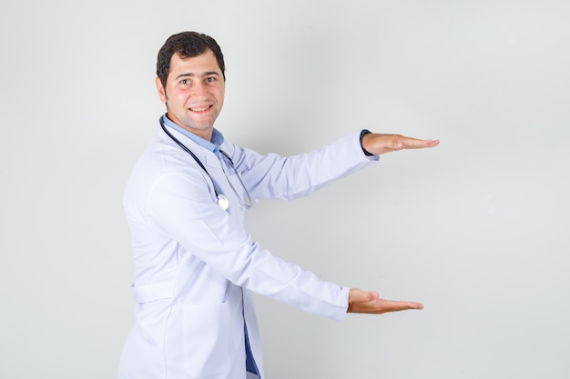 Médecin de sexe masculin montrant un signe de grande taille en blouse blanche et à la joyeuse vue de face.