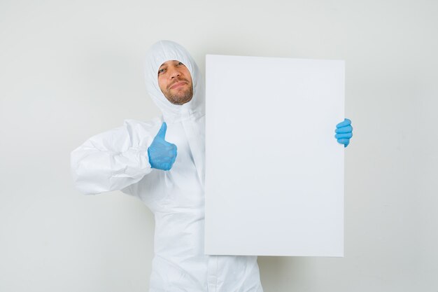 Médecin de sexe masculin tenant un tableau blanc avec le pouce vers le haut en tenue de protection