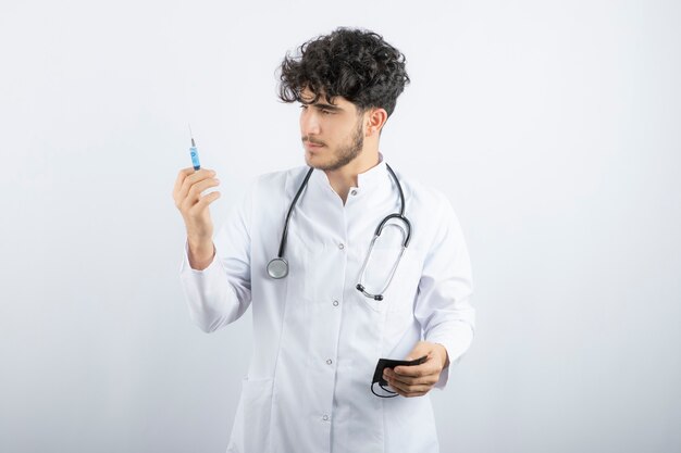 Médecin de sexe masculin en uniforme blanc avec stéthoscope tenant une seringue.