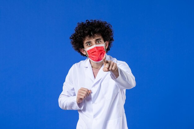 Médecin de sexe masculin vue de face en costume médical avec masque rouge sur bleu