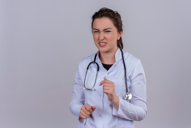 Médecin squeamish jeune fille portant une blouse médicale portant un stéthoscope sur fond blanc