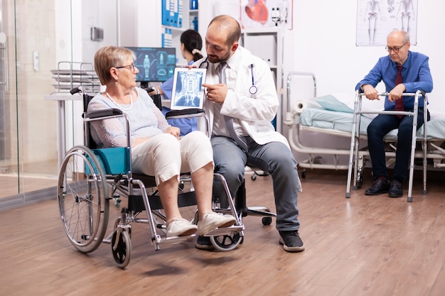 Médecin avec stéthoscope à l'aide de tablet pc lors de l'examen d'une femme handicapée en fauteuil roulant