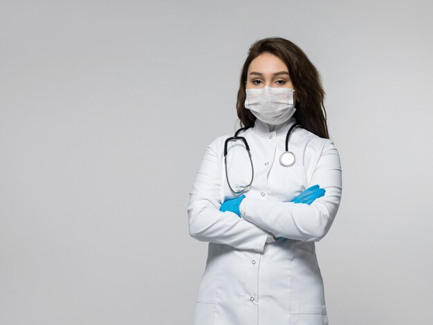 Médecin avec stéthoscope en uniforme médical blanc, portant des gants bleus et un masque stérile blanc