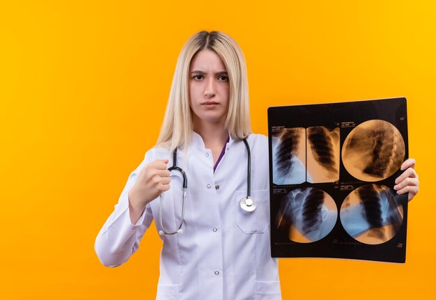 Médecin strict jeune fille portant un stéthoscope en robe médicale tenant x-ray sur fond jaune isolé