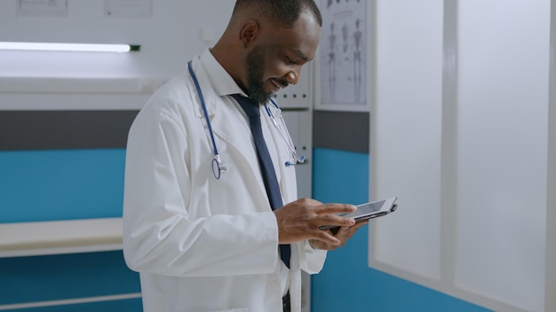 Médecin thérapeute spécialiste afro-américain analysant le rapport de maladie à l'aide d'un ordinateur tablette travaillant au traitement médicamenteux dans le bureau de l'hôpital. homme médecin tapant une mauvaise expertise. notion de médecine