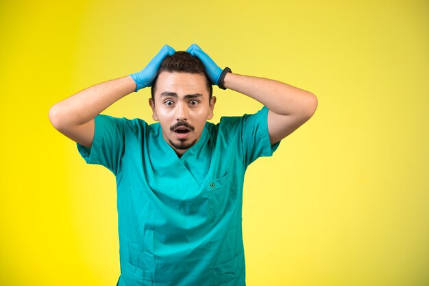 Médecin en uniforme vert et masque à la main frustré et confus.