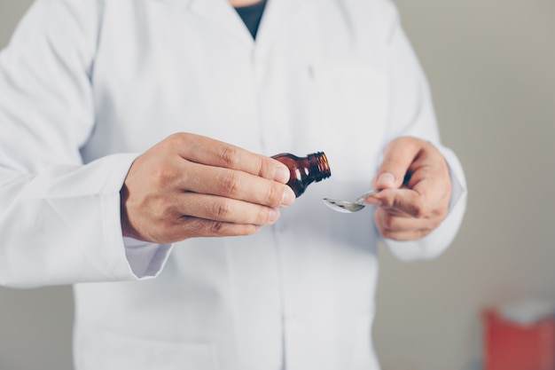 Un médecin verse du sirop pour quelqu'un, vue de côté.