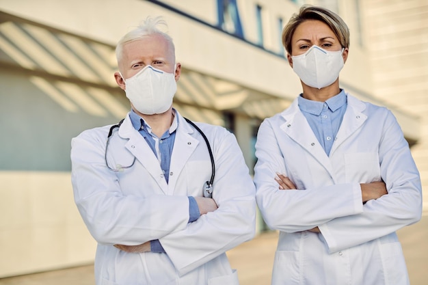 Médecins confiants avec des masques protecteurs debout avec les bras croisés à l'extérieur