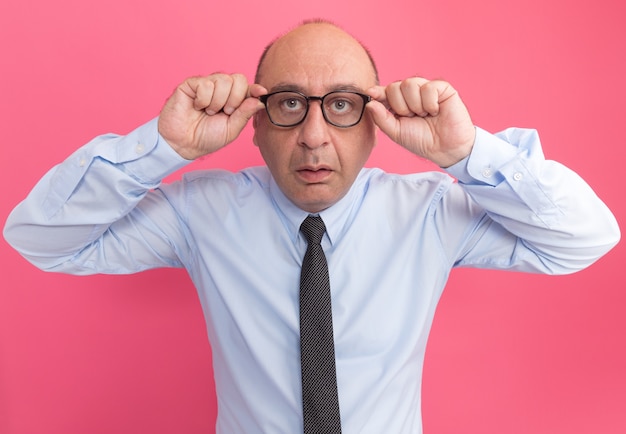 Méfiant à l'avant homme d'âge moyen portant un t-shirt blanc avec cravate et lunettes isolé sur mur rose