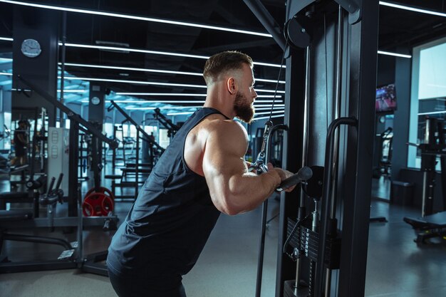 Meilleur choix. Jeune athlète caucasien musclé s'entraînant dans une salle de sport, faire des exercices de force, pratiquer, travailler sur le haut de son corps avec des poids et des haltères. Fitness, bien-être, concept de mode de vie sain.