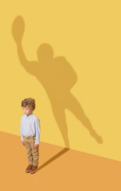 Meilleur membre de l'équipe. Concept d'enfance et de rêve. Image conceptuelle avec enfant et ombre sur le mur jaune du studio. Le petit garçon veut devenir joueur de football américain et se bâtir une carrière sportive.