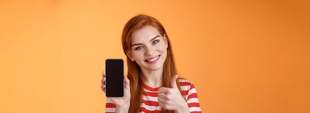 Photo gratuite la meilleure application pour smartphone garantit une belle femme rousse à l'air amicale et affirmée recommande une application pour téléphone portable