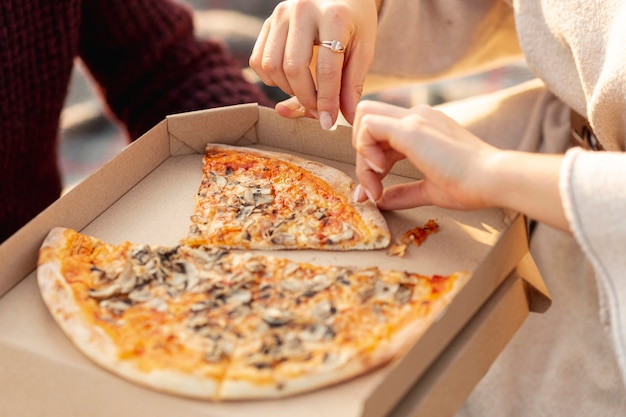 Les meilleurs amis au grand angle savourant une pizza ensemble à l'extérieur