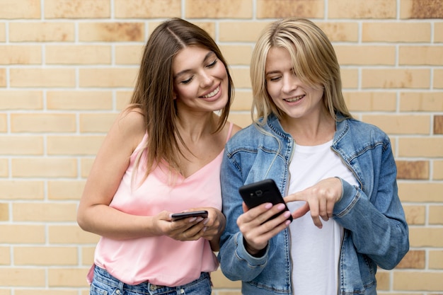 Photo gratuite meilleurs amis à la recherche de leurs téléphones portables à l'extérieur