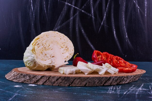 Mélange de légumes sur un plateau en bois avec du poivre et du chou sur l'espace bleu.