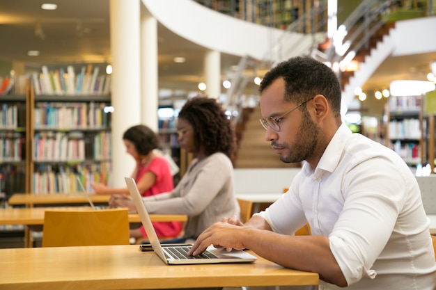 Mélanger des stagiaires racés travaillant sur ordinateur dans une bibliothèque publique
