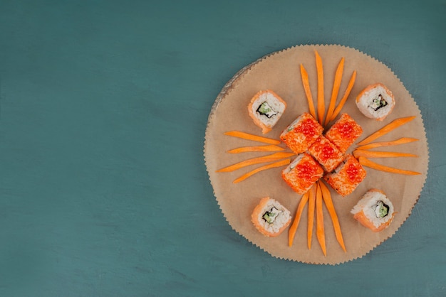 Photo gratuite mélanger les sushis avec des tranches de carottes sur une planche de bois.