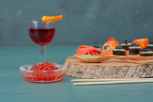 Mélangez des sushis, du caviar rouge et un verre de vin rouge sur une table bleue.