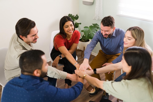 Les membres d'un groupe de soutien joignent leurs mains pour faire un high five. Jeunes femmes et hommes joyeux célébrant leur séance de conseil réussie