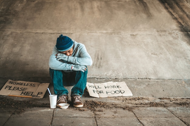 Les mendiants assis sous un pont avec des tasses ont de l'argent.