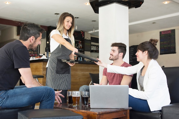 Menu de présentation de serveuse à une cliente avec des amis au bar