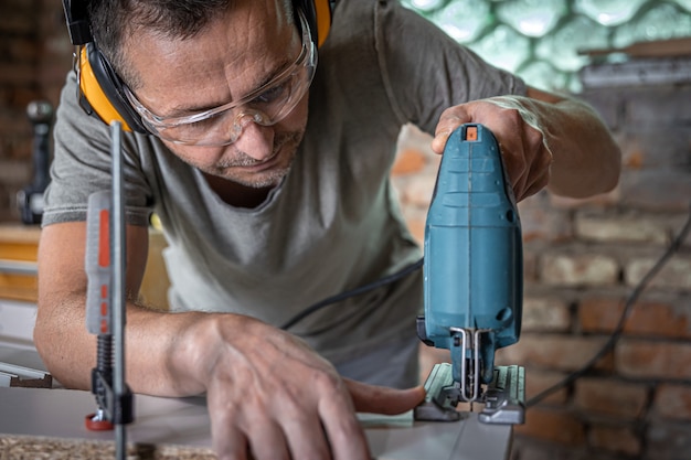 Un menuisier caucasien se concentre sur la coupe du bois avec une scie sauteuse dans son atelier.