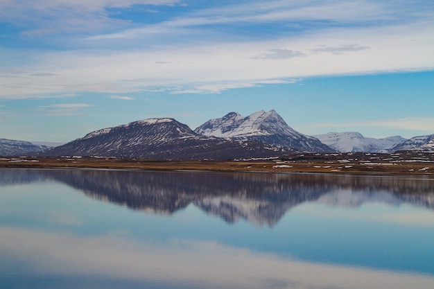 Mer entourée de montagnes rocheuses couvertes de neige et se reflétant sur l'eau en Islande