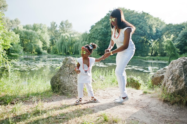 Mère afro-américaine avec sa fille au lac de fond de robes blanches au parc