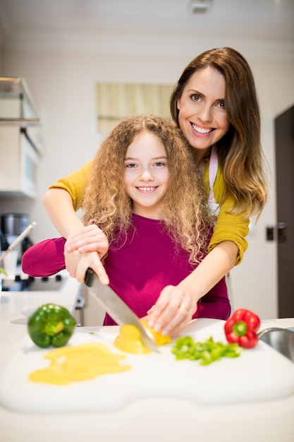 Mère d&#39;aider sa fille à couper les légumes dans la cuisine