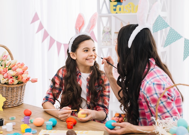 Mère appliquant la couleur au nez de sa fille tout en décorant les oeufs de Pâques